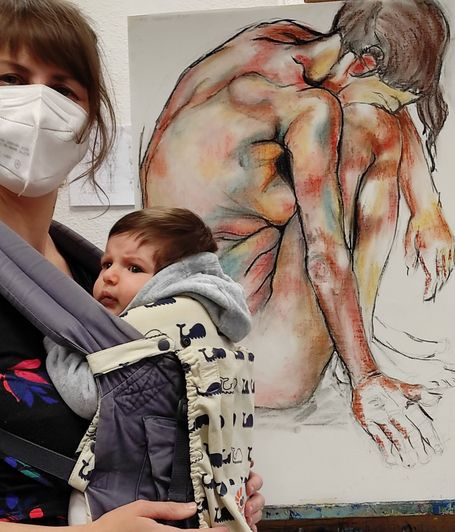 pintora posando con mascarilla y su bebé, con una pintura de una mujer desnuda de fondo