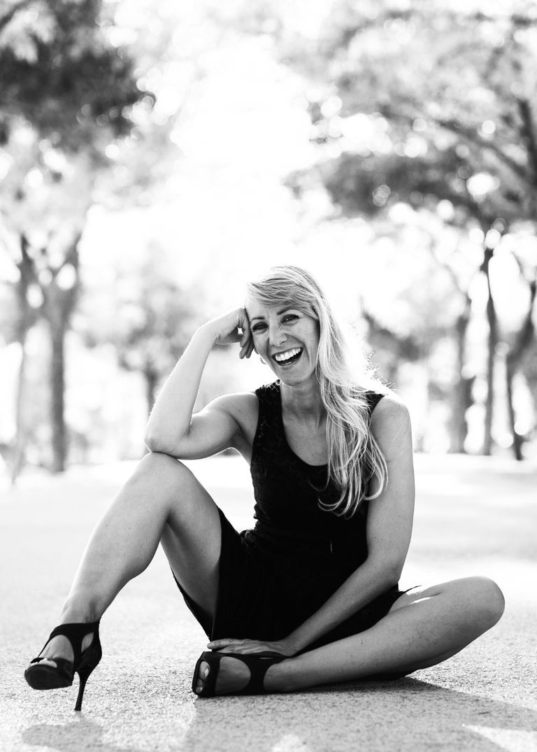 Mujer posando sentada con un vestido negro y tacones sonriendo