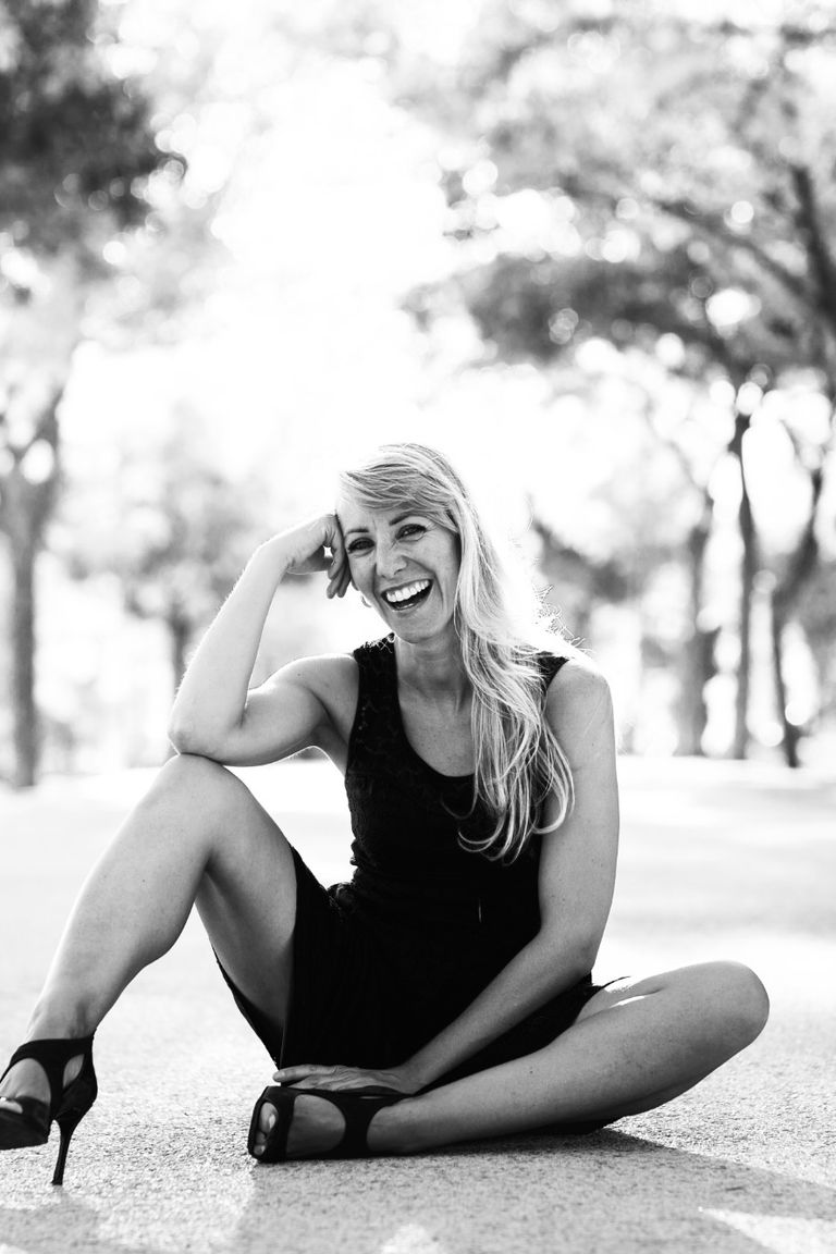 Mujer pintora sentada en el suelo con un vestido negro y tacones sonriendo