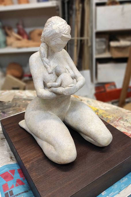 Escultura de una mujer desnuda de rodillas con su bebé en brazos