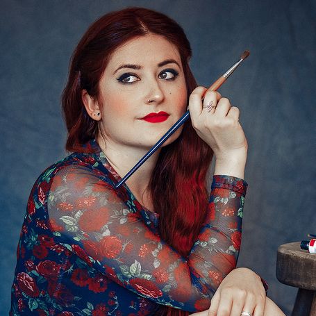 Ilustradora pelirroja de pelo largo posando con su pincel