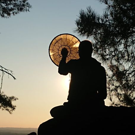 Chamán a contraluz con un instrumento mirando al horizonte