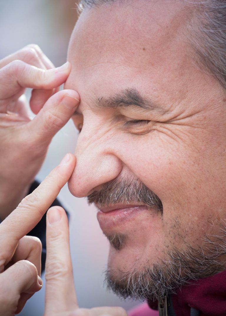 Hombre sonriendo con dedos de otras personas que le tocan la cara